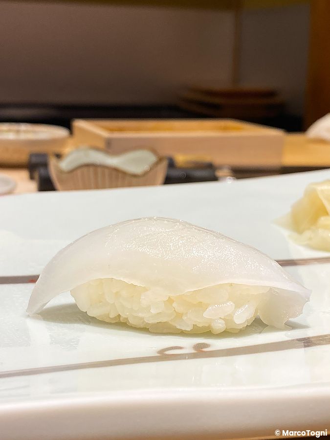 Un nigiri di ika bianco posato su un piatto di ceramica chiara all'interno del ristorante Ginza Kyubey a Tokyo.