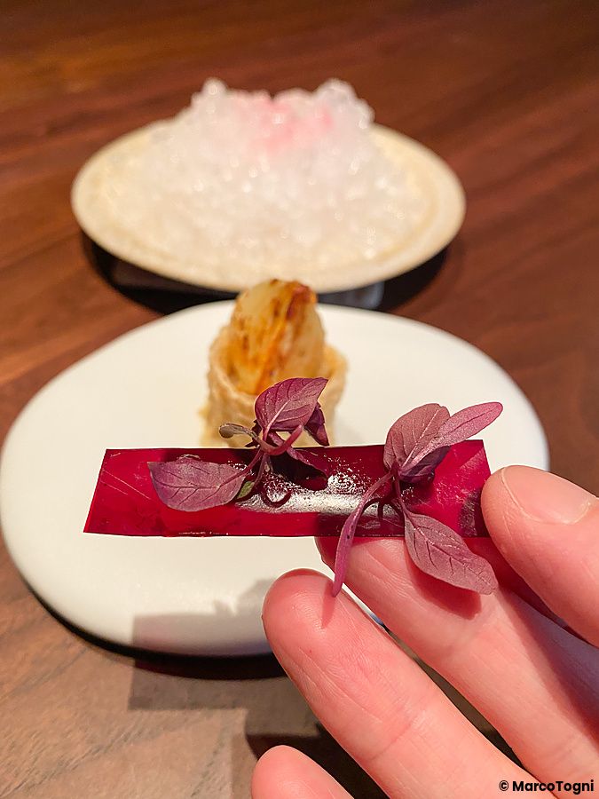Una mano sostiene un foglio di barbabietola con tofu fermentato e fiori di amaranto al ristorante La Cime di Osaka.