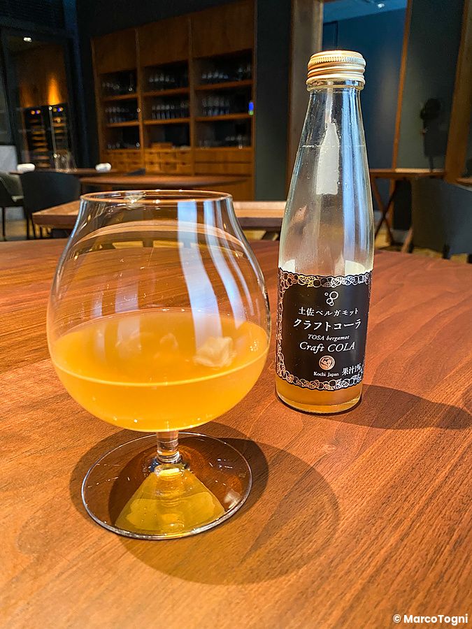 Una bottiglia di cola artigianale e un calice con liquido ambrato su un tavolo in legno presso il ristorante La Cime.