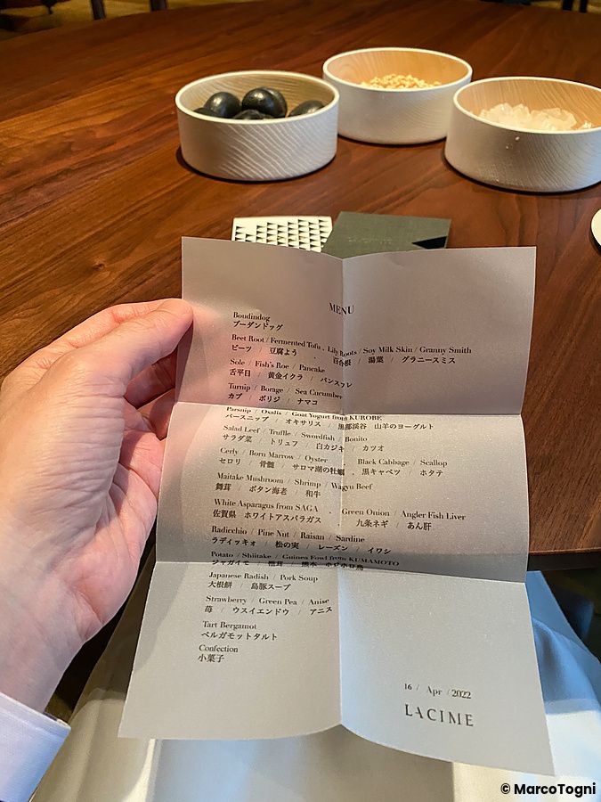 Una mano tiene il menu cartaceo del ristorante La Cime ad Osaka con l'elenco delle portate.