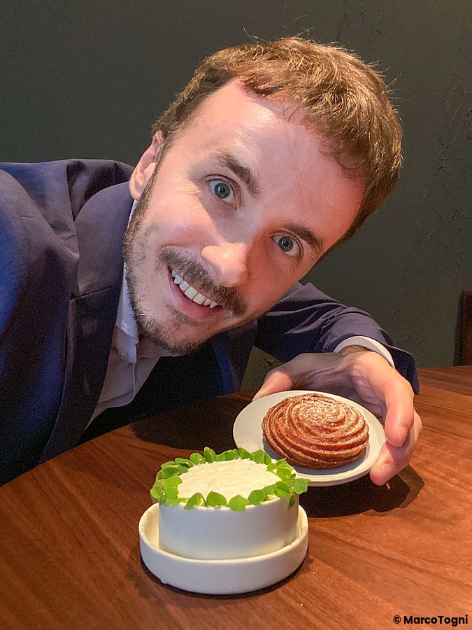 Marco Togni sorridente tiene davanti a sé una ciotola con yogurt di capra e pastinaca con ossalide e una girella salata.