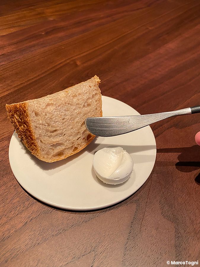 Pane e burro di soia. a La Cime serviti su un piccolo piatto bianco su un tavolo di legno scuro.