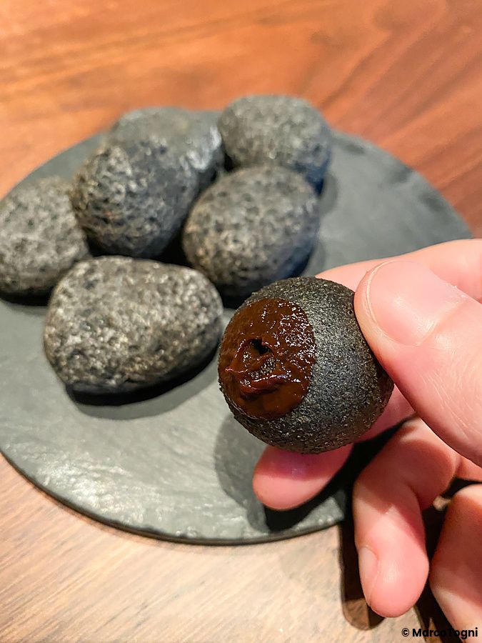 Un primo piano di una mano che tiene un sasso commestibile al budin noir e carbone vegetale presso il ristorante La Cime.