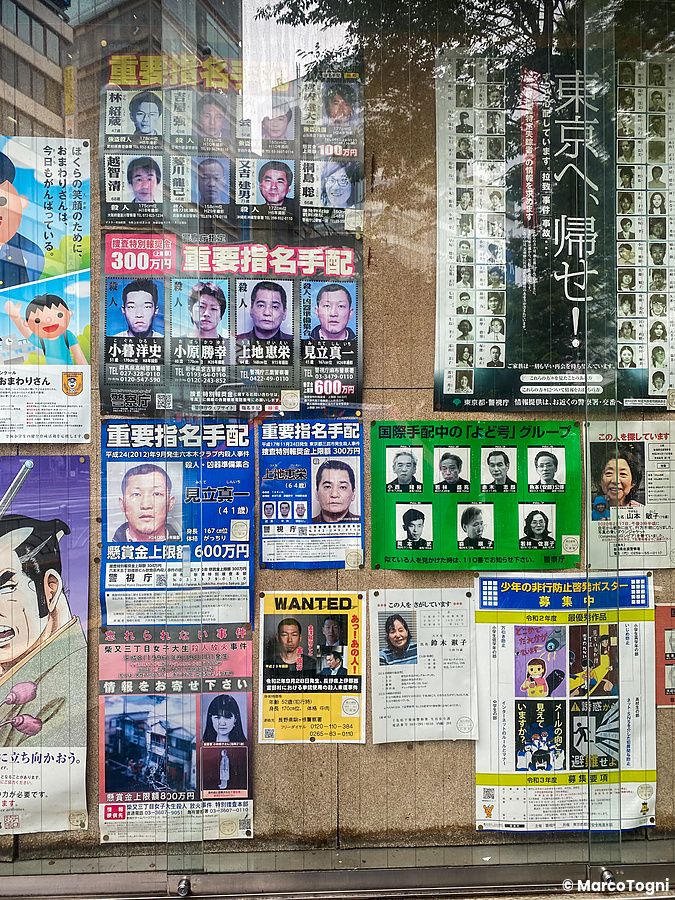Una bacheca piena di manifesti della polizia con foto di ricercati e avvisi di persone scomparse a Tokyo.
