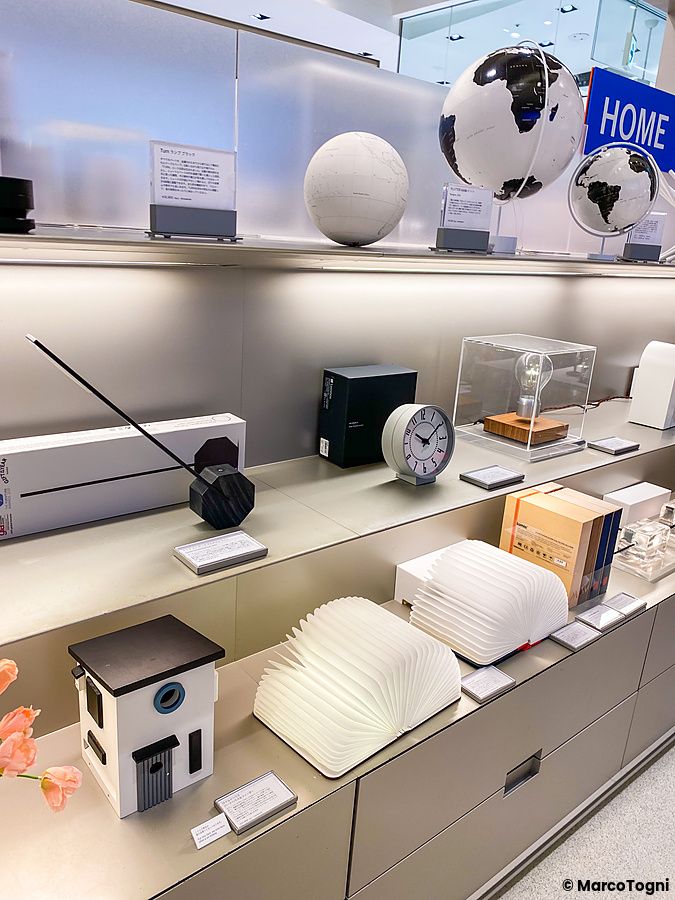 Ripiani metallici nel Moma Design Store a Tokyo con globi, lampade, orologi e libri luminosi in vendita.