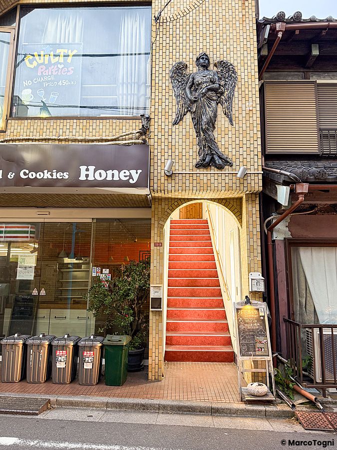 L'ingresso a Ristorante Momose Shokudo presenta una scala con moquette rossa sotto una scultura di un angelo.