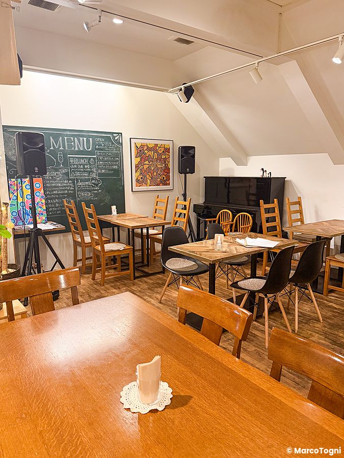 Interno del ristorante a Ristorante Momose Shokudo con tavoli in legno, sedie e una lavagna con menu a parete.