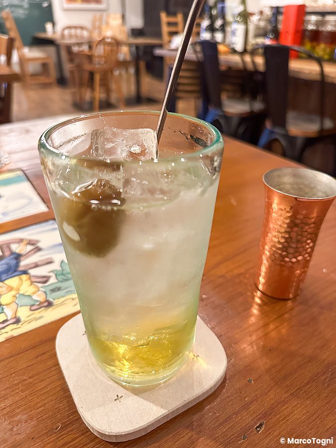 Un bicchiere di umeshu con ghiaccio e una prugna al Ristorante Momose Shokudo poggiato su un tavolo di legno.
