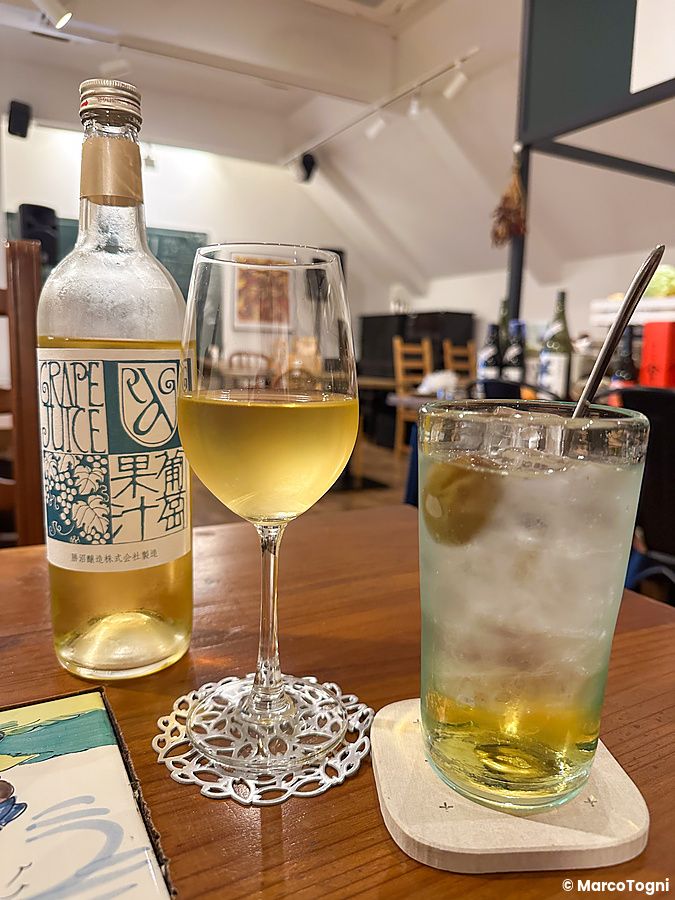 Calice di vino bianco e bicchiere di umeshu su un tavolo al Ristorante Momose Shokudo.