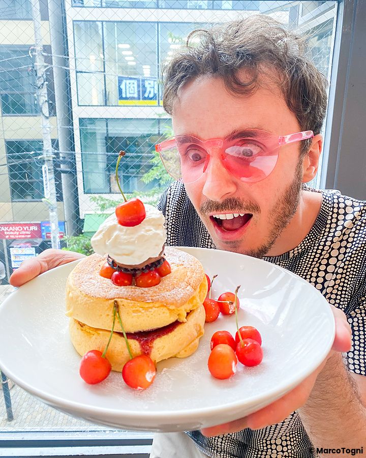 Marco Togni con occhiali rosa tiene un piatto di pancake con ciliegie da Flipper's