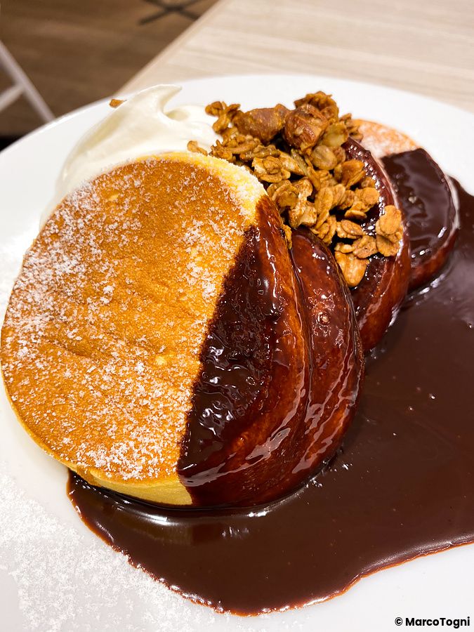 Un piatto di a Happy Pancake guarnito con salsa al cioccolato, granella croccante e panna montata.