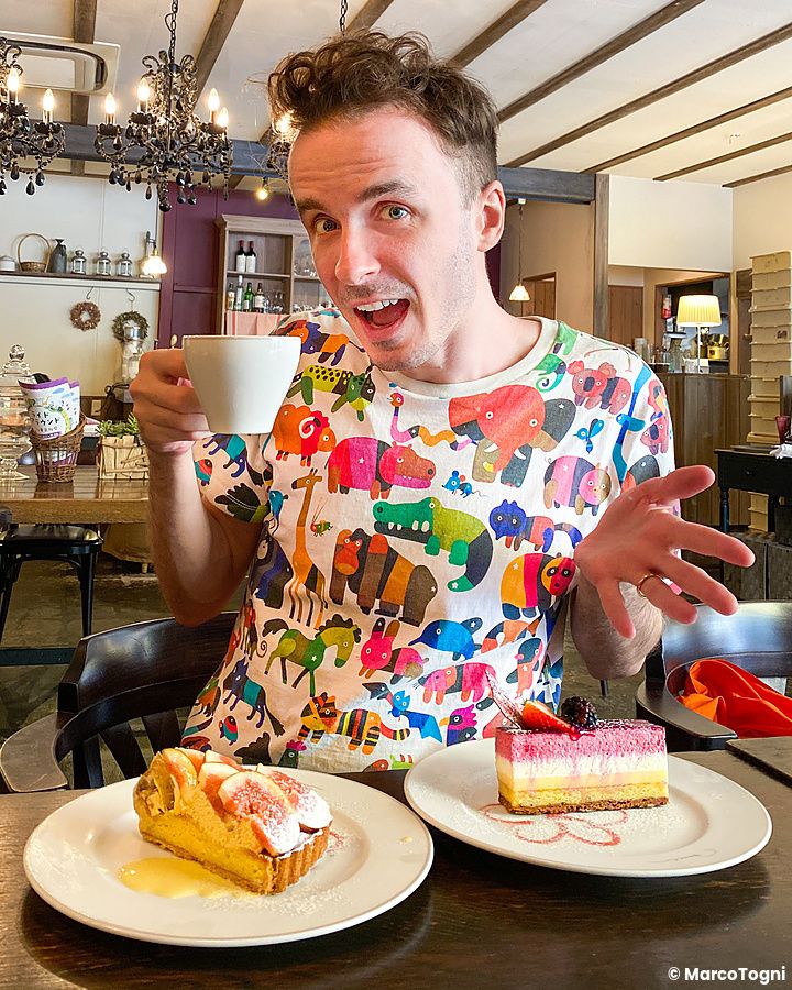 Marco Togni con una maglietta colorata è seduto a un tavolo della pasticceria Basel ad Hachioji con davanti due dolci.