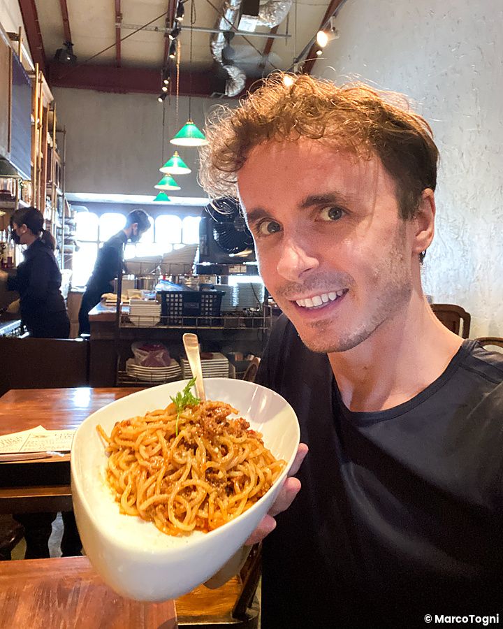 Marco Togni sorride tenendo un piatto di pasta in mano all'interno del ristorante Cocktail Works a Karuizawa.