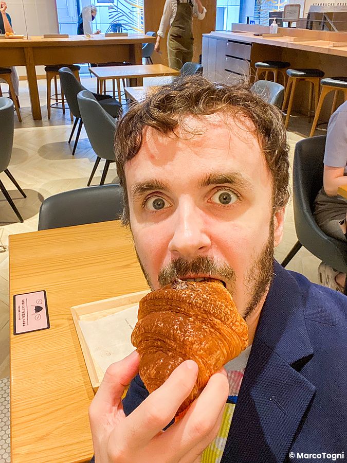 Marco Togni mangia un cornetto seduto a un tavolo all'interno dello Starbucks Reserve a Ginza.