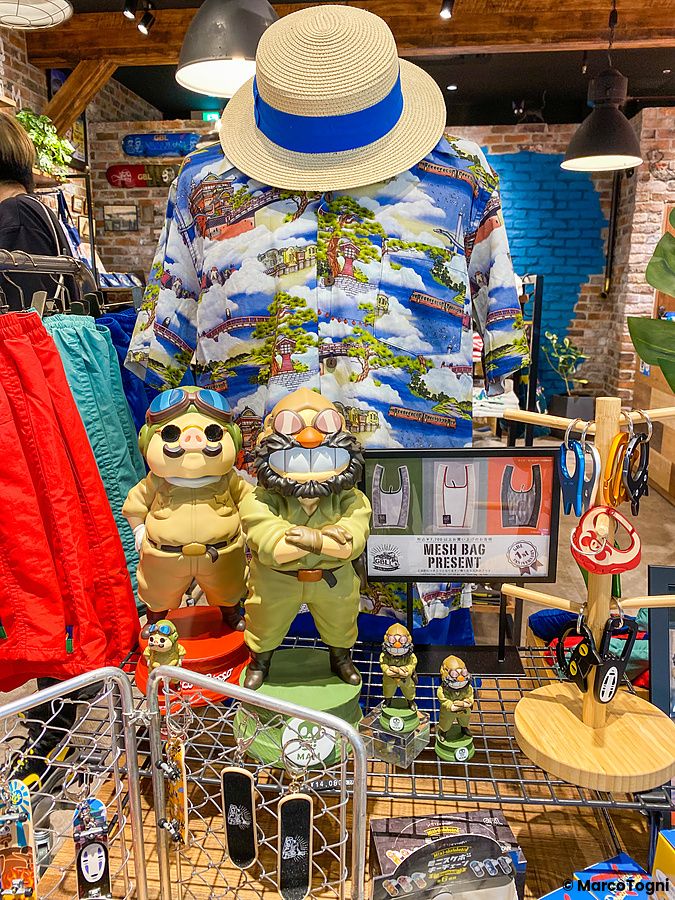 Interno di un negozio di Studio Ghibli a Tokyo con statuette di personaggi, una camicia stampata e un cappello di paglia.