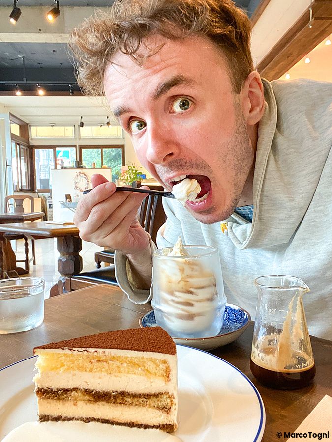 Marco Togni mangia un dessert in un bicchiere all'interno del Takao Coffee, con una fetta di torta sul tavolo in primo piano.