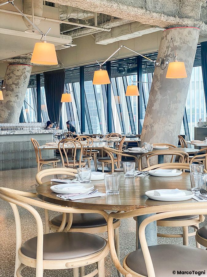 Interno del ristorante The Apollo a Ginza a Tokyo con tavoli in legno, sedie circolari e colonne in cemento.