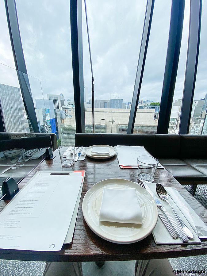 Tavolo apparecchiato presso il ristorante The Apollo a Ginza con vetrate che offrono una vista panoramica su Tokyo.