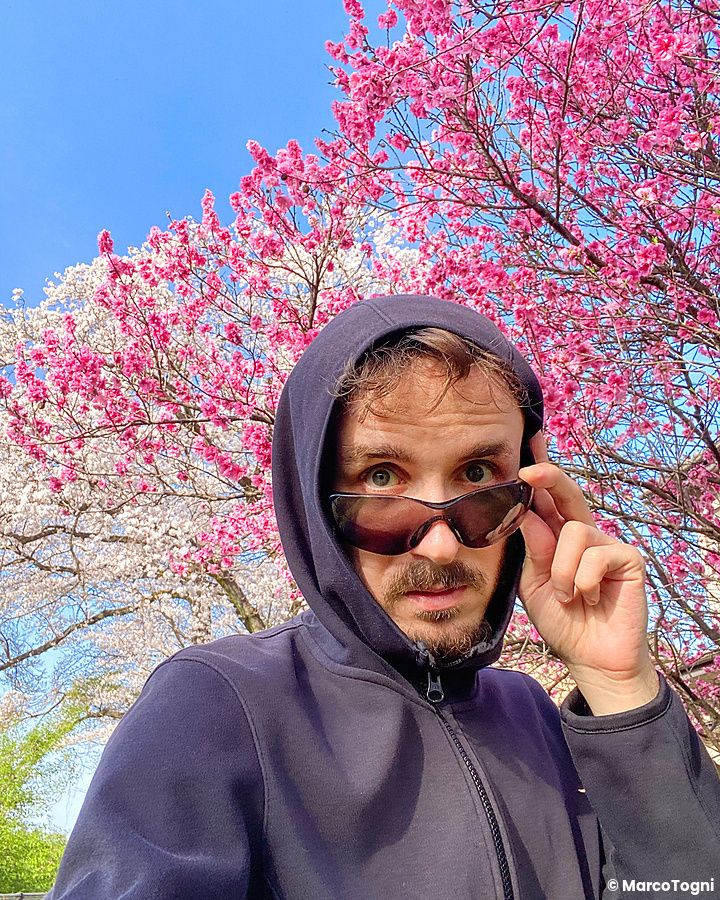 Marco Togni con occhiali da sole davanti a ciliegi in fiore a Tokyo.