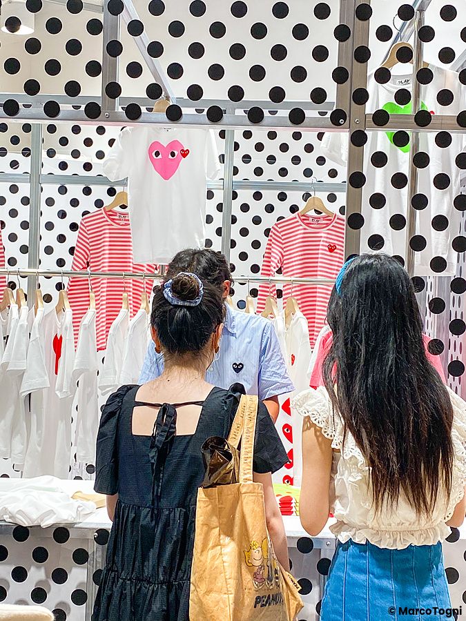 Interno del Moma Design Store a Tokyo con esposizione di abiti Comme des Garçons e tre persone che osservano i capi.