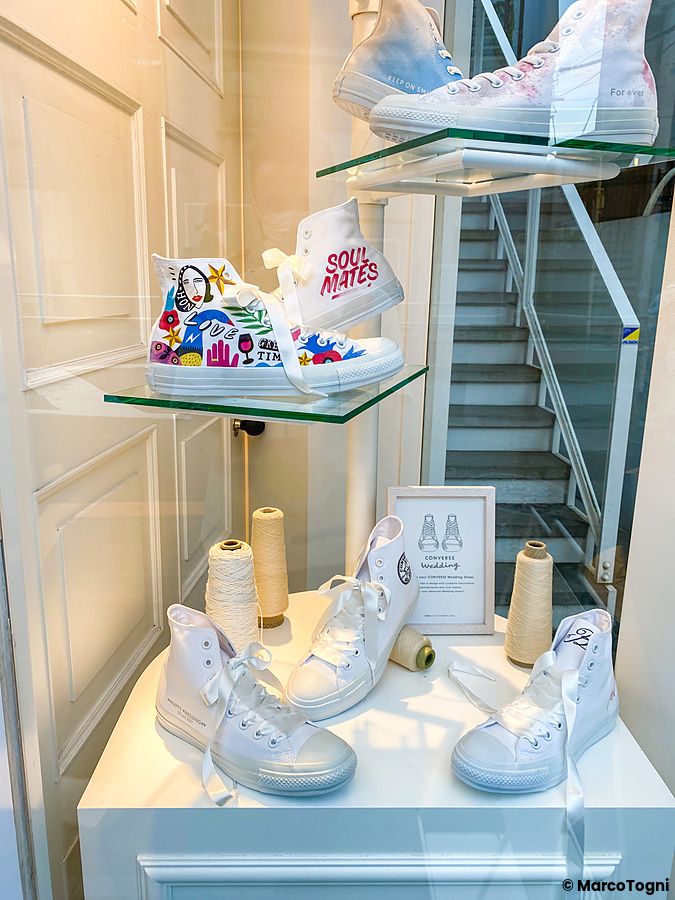 Vetrina di un negozio a Tokyo con diverse paia di scarpe Converse bianche esposte su ripiani di vetro.