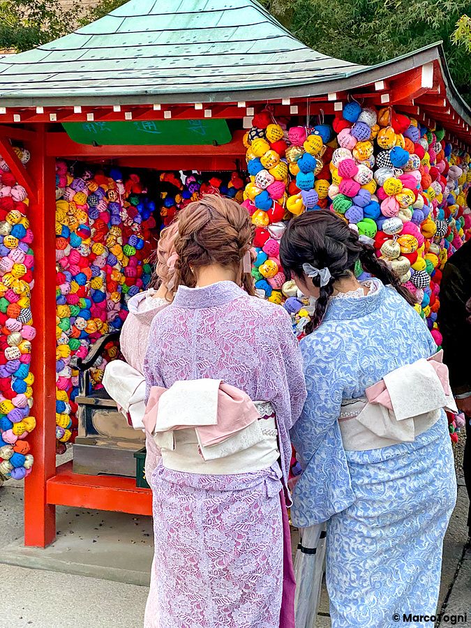 Persone in kimono osservano kukurizaru colorati al Yasaka Koshindo, Kyoto.