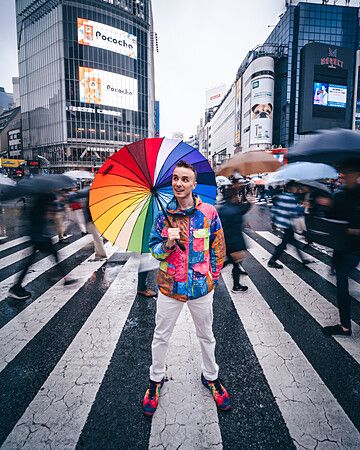 Marco Togni con ombrello arcobaleno a Shibuya, Tokyo, in un incrocio trafficato
