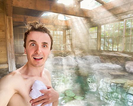 Marco Togni sorridente in un onsen a Yufuin con luce solare e vapore