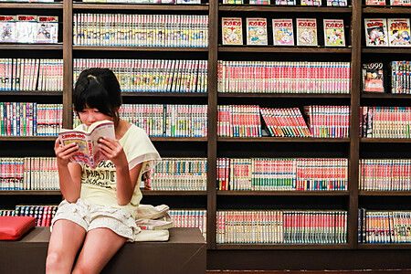 Ragazza che legge un manga davanti a scaffali pieni di volumi al Museo di Manga.