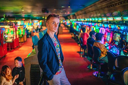 Marco Togni in una sala pachinko luminosa con altre persone alle macchine.