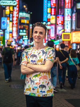 Marco Togni sorridente con maglietta colorata tra le luci al neon di Shibuya.