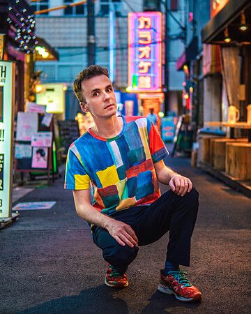 Marco Togni accovacciato in una strada di Shimokitazawa con luci al neon.