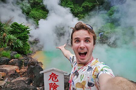 Marco Togni sorridente scatta un selfie davanti a una sorgente termale fumante.