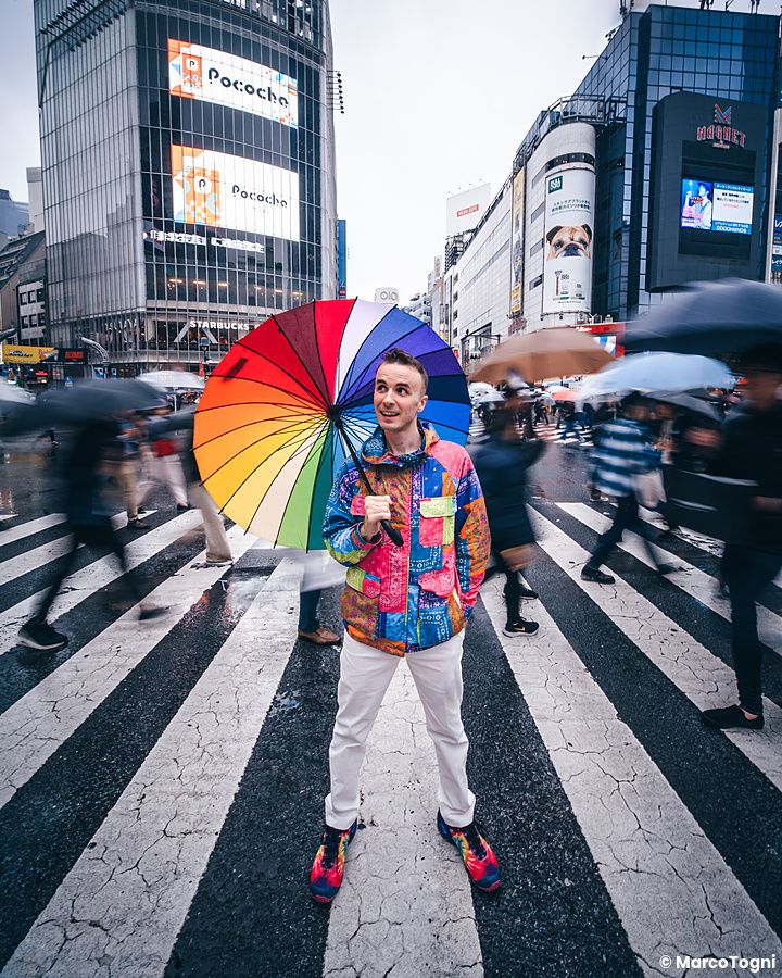 Marco Togni con ombrello arcobaleno a Shibuya, Tokyo, in un incrocio trafficato