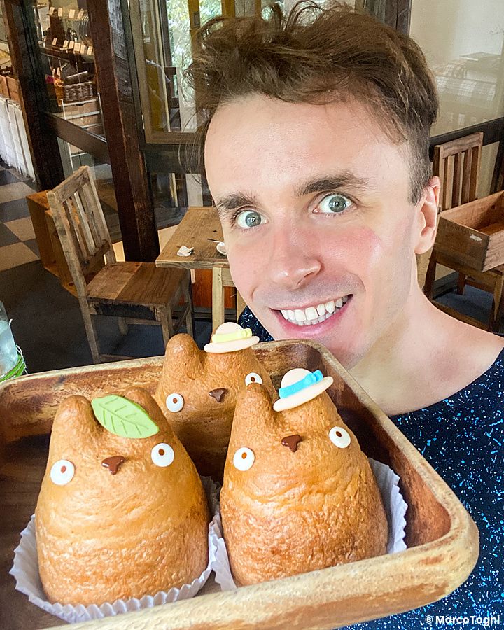 Marco Togni sorride tenendo un vassoio con tre bignè a forma di Totoro all'interno di Shiro Hige Cream Puff a Tokyo.