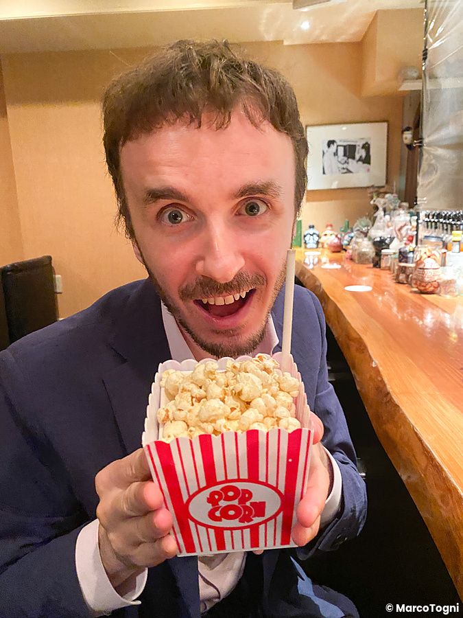 Marco Togni sorridente tiene in mano una scatola di popcorn con un cocktail nascosto all'Orchard Bar di Ginza, Tokyo.