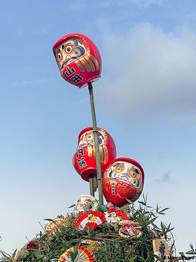 Tre bambole Daruma rosse montate su un supporto di bambù durante il tradizionale evento dondoyaki in Giappone.