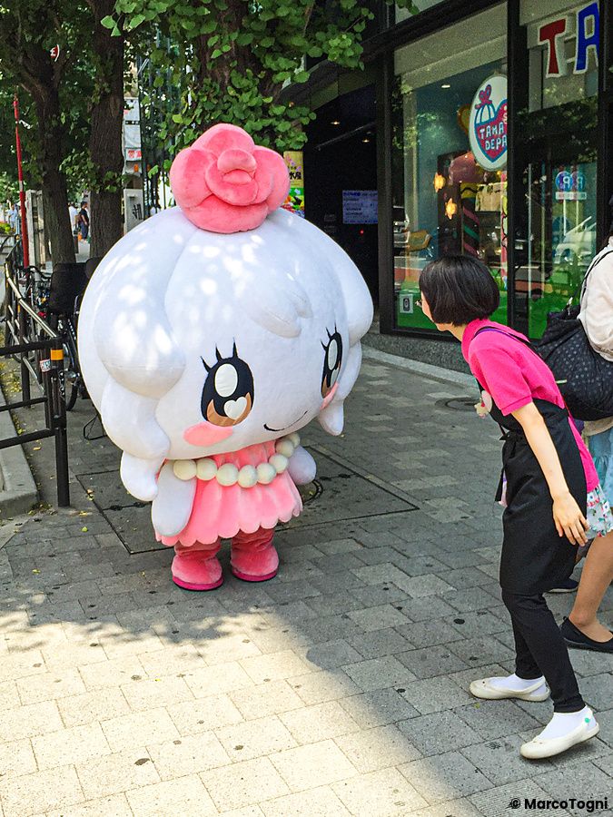 Persona interagisce con mascotte kawaii in strada a Tokyo.