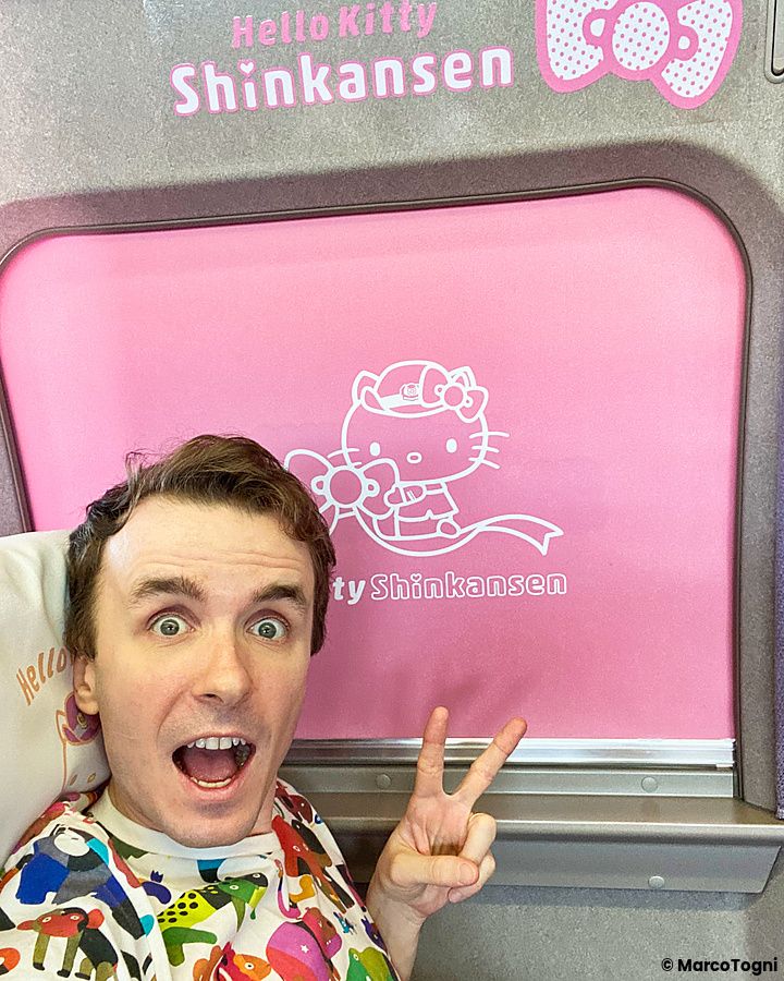 Marco Togni si scatta un selfie all'interno dello shinkansen di Hello Kitty davanti a una tendina rosa del treno.