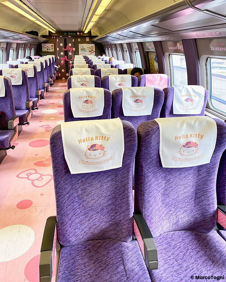 Interno del treno shinkansen di Hello Kitty con sedili viola e decorazioni a tema.