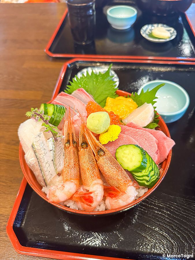 Una ciotola di kaisendon con pesce crudo, gamberi e riso servita su un vassoio nero laccato.