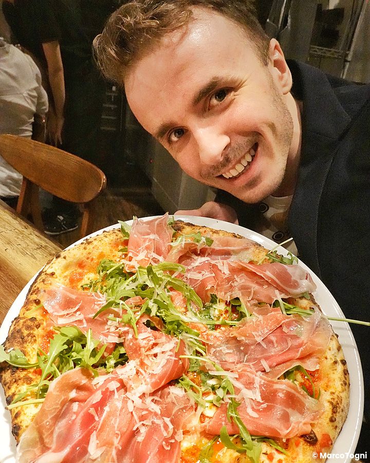 Marco Togni sorridente con pizza al prosciutto e rucola alla pizzeria Da Take.