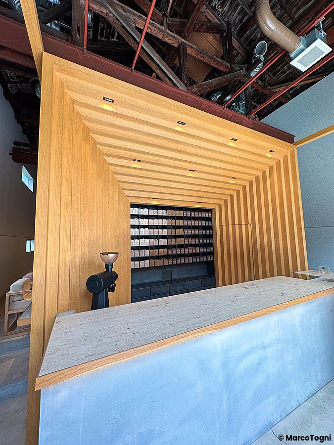 Veduta interna di Koffee Mameya Kakeru a Tokyo con bancone in pietra e una parete espositiva in legno per il caffè.