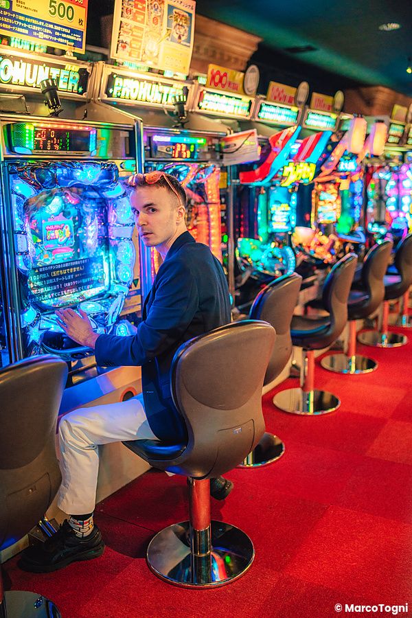 Marco Togni che gioca a pachinko in una sala illuminata da luci al neon.