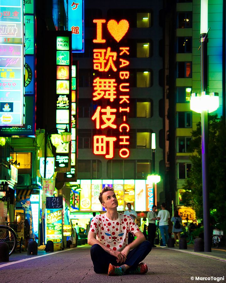 Persona seduta per strada a shinjuku davanti a insegne al neon di kabukicho