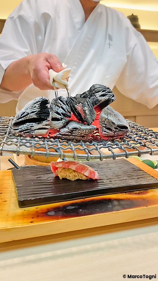 Un sushi scaldato da carboni ardenti sopra una griglia metallica gestita da uno chef al ristorante Sushi Tou a Tokyo.