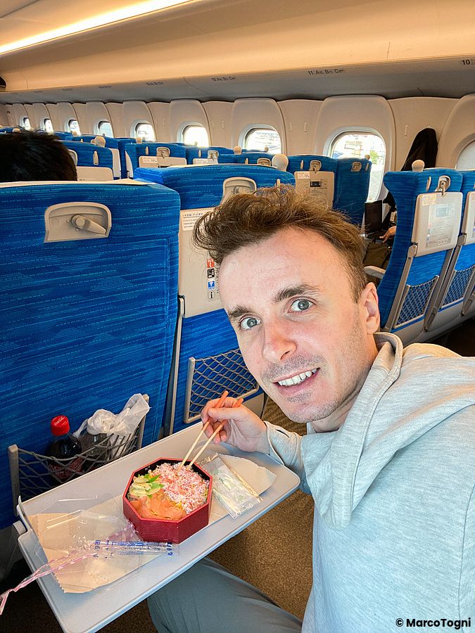Marco Togni sul treno Shinkansen con cibo tra le mani.