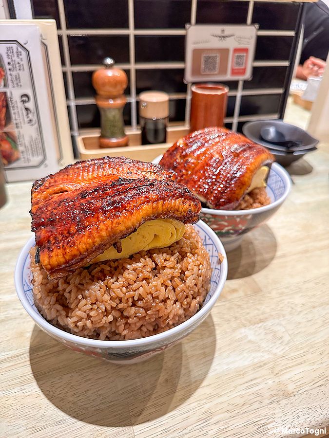 Due ciotole di riso con unagi e tamagoyaki servite su un bancone di legno all'interno del ristorante Izumo a Osaka.