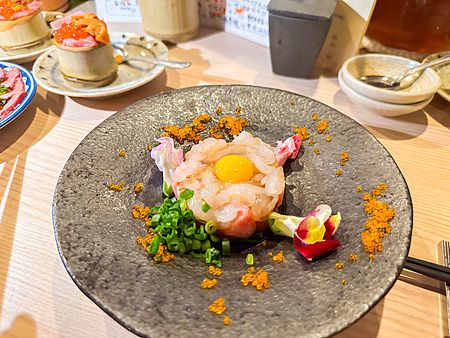 Un crudo di mare a Shibuya Kito Kito servito in un piatto di ceramica scura con tuorlo d'uovo, uova di pesce e fiori.