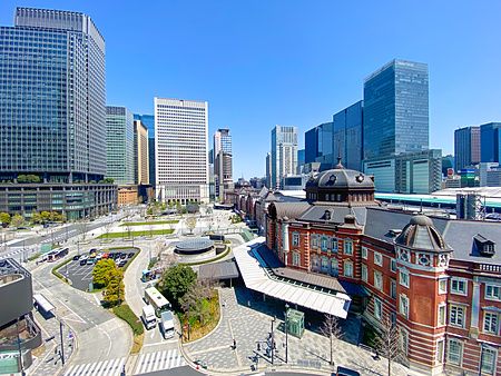 Veduta dall'alto della stazione di Tokyo con il suo edificio storico in mattoni rossi circondato da moderni grattacieli.